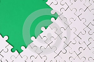 Fragment of a folded white jigsaw puzzle on the background of a green plastic surface. Texture photo with copy space for text