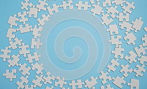 Fragment of a folded white jigsaw puzzle and a pile of uncombed puzzle elements against the background of a blue surface