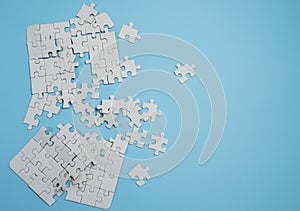 Fragment of a folded white jigsaw puzzle and a pile of uncombed puzzle elements against the background of a blue surface