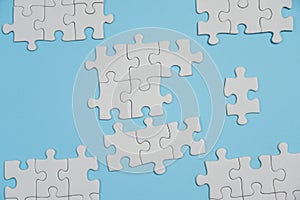 Fragment of a folded white jigsaw puzzle and a pile of uncombed puzzle elements against the background of a blue surface