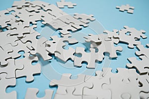 Fragment of a folded white jigsaw puzzle and a pile of uncombed puzzle elements against the background of a blue surface