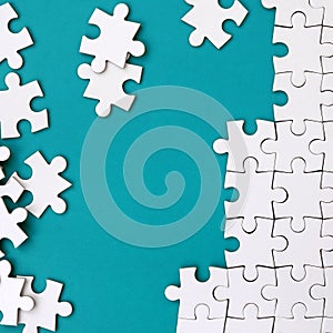 Fragment of a folded white jigsaw puzzle and a pile of uncombed puzzle elements against the background of a blue surface. Texture