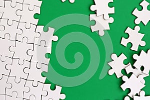 Fragment of a folded white jigsaw puzzle and a pile of uncombed puzzle elements against the background of a green surface. Texture