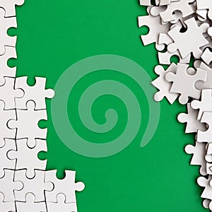 Fragment of a folded white jigsaw puzzle and a pile of uncombed puzzle elements against the background of a green surface. Texture