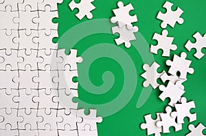 Fragment of a folded white jigsaw puzzle and a pile of uncombed puzzle elements against the background of a green surface. Texture