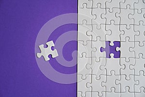 Fragment of a folded white jigsaw puzzle and a pile of uncombed puzzle elements against the background of a Violet surface