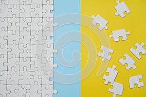 Fragment of a folded white jigsaw puzzle and a pile of uncombed puzzle elements against the background of a yellow surface