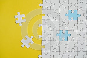 Fragment of a folded white jigsaw puzzle and a pile of uncombed puzzle elements against the background of a yellow surface