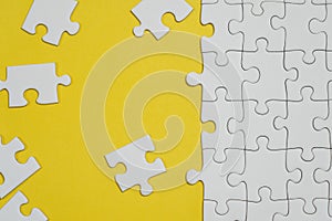 Fragment of a folded white jigsaw puzzle and a pile of uncombed puzzle elements against the background of a yellow surface