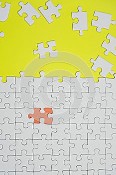 Fragment of a folded white jigsaw puzzle and a pile of uncombed puzzle elements against the background of a yellow surface