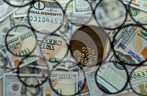 A fragment of a gold bar in a circle against the background of round fragments of hundred-dollar bills.