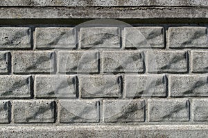 A fragment of gray concrete relief wall or fence imitating several rows of rectangular bricks laid horizontally
