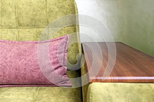 Fragment of a green sofa with a wooden armrest and a pink pillow