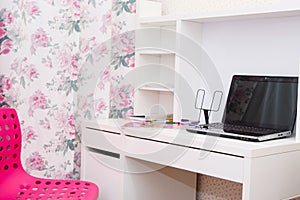 A fragment of the interior of a children`s room with a work Desk, textbooks and a laptop. Pink curtains on the Windows