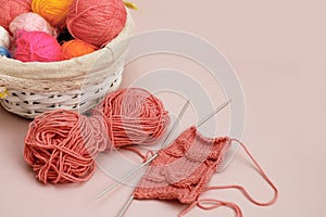 a fragment of knitting with a pattern on knitting needles next to a basket with multi-colored balls of thread
