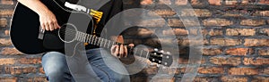 Fragment man play a black acoustic guitar on a old brick wall background