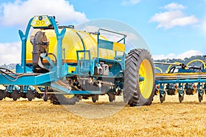 A fragment of a modern agricultural seeder against a yellow field and a blue sky