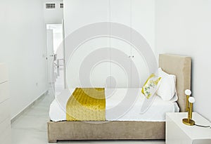 Fragment of modern bedroom in minimalist white and yellow interior design style with built-in closet. Bed with pillows duvet