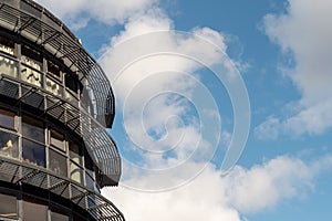 Fragment of modern building with metal and glass elements against blue cloudy sky. Round shape of the building. Advanced