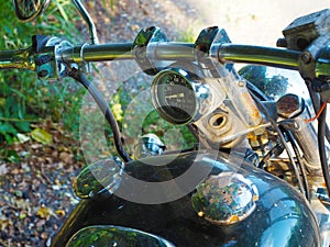 Fragment of a motorcycle with a rusting handlebar and speedometer on it and rust-covered caps on the gas tank
