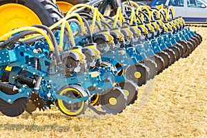 A fragment of a multi row seeder against the background of an agricultural field on a sunny day