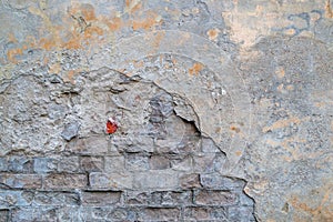 Fragment of old brick wall with partially collapsed cracked gray cement plaster, brickwork is visible where is facing damage