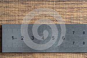 Fragment of a old metal ruler on wooden background, macro. Industrial steel ruler in centimeters, closeup