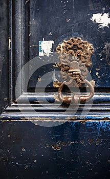 Rusty forged metal door handle with a patterned base on a dark blue old flaky front door