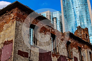 Fragment of an old ruined brick building against the background of a fragment of the glass facade of an office building