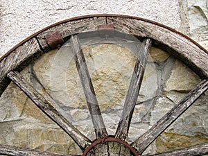 Fragment of an old wooden cartwheel against a wall of natural stone.