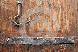 Fragment of an old wooden gate painted brown with a rusty metal plank and a locking hook