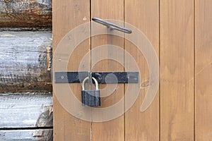 A fragment of an old wooden hut with a door. An old wooden door for entering and exiting the house,locked with a padlock