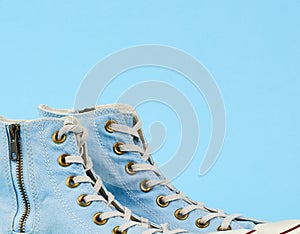 Fragment of a pair of light blue worn textile sneakers with laces and zippers