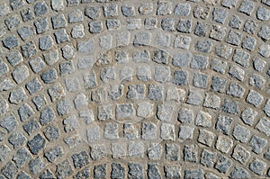 Fragment of pavement paved with rough square gray stone blocks with uneven edges in the form of semicircular arched streaks