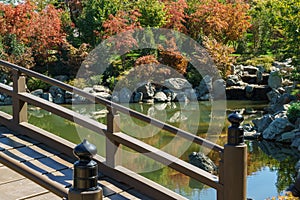 Fragment of picturesque wooden pedestrian bridge across large lake Oike in Japanese garden. Public landscape park