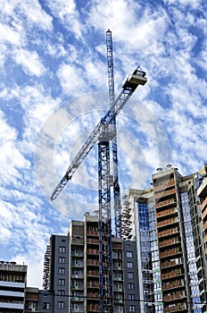 A fragment of a residential building under construction and high-rise cranes against a bright cloudy sky