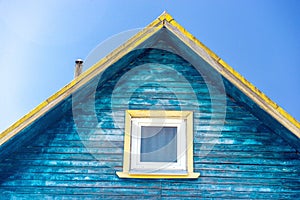 Fragment of roof of old wooden house with iron chimney and plastic window with white frame. Holes and gaps between boards. Rustic