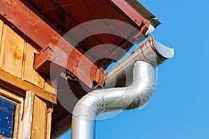 Fragment of the roof of a village house with drainpipe closeup against blue sky