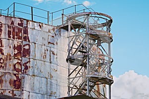 Fragment of a rusty tank farm for storing petroleum products with a ladder. An old above ground storage tank for liquid