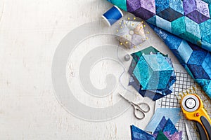 Fragment of tumbling blocks quilt, accessories for quilting on a white surface. Space for text