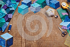 Fragment of tumbling blocks quilt, accessories for quilting on a wooden surface. Space for text