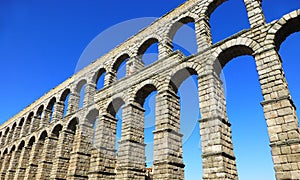 A fragment of a two-tiered aqueduct arcade against the backdrop of the bright blue sky of Spain