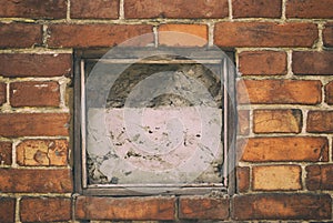 Fragment of the wall of an old house with a bricklaying of red brick and concreted a small window in the center