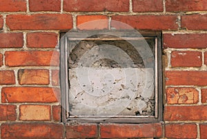 Fragment of the wall of an old house with a bricklaying of red brick and concreted a small window in the center