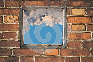 Fragment of the wall of an old house with a bricklaying of red brick and and view from small window with cloud sky