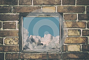 Fragment of the wall of an old house with a bricklaying of red brick and and view from small window with cloud sky