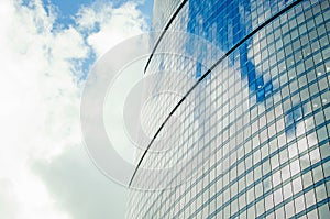 Fragment of a wall of a skyscraper with mirror glass against a sky with clouds.