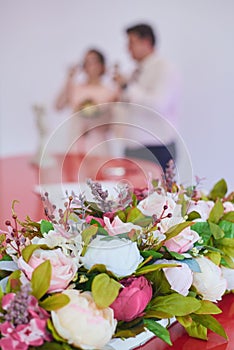 A fragment of a wedding decoration - rose flowers, the bride and groom drink champagne in the background, out of focus