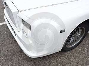 Fragment of a white matte car with square headlights and cracks on the body. Closeup photo