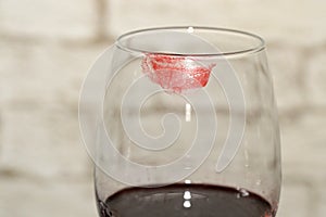 A fragment of a wine glass with a red lipstick marks..